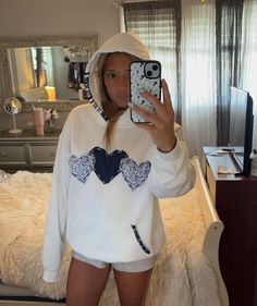 a woman taking a selfie in her bedroom wearing a white hoodie and shorts