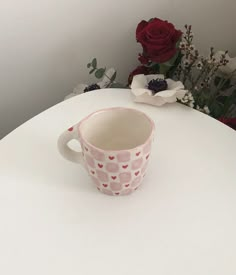 a coffee cup sitting on top of a white table next to red roses and other flowers