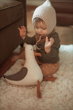 a small child sitting on the floor next to a stuffed bird and pointing at it