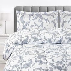 a white and blue comforter set on a bed with two lamps in the background