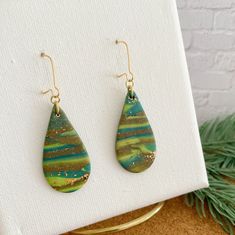 Stylish teardrop earrings in shades of green. These evergreen forrest earrings are a great statement piece to add sophistication to a simple outfit or pair with anything. Our evergreen Earrings are handcrafted in polymer clay and fired to create a beautiful piece that will last for years. The lightweight design adds a mix of fun and sophistication, with a twist. SPECS: Do you want to stand out from the crowd?  Wear these liquid art earrings that are: - Durable and lightweight - Handmade with care from polymer clay - Each one is unique - gold tone ear wires - Each earring is baked, sanded, drilled, and assembled by me with love Keep your jewelry collection light and bright with these earrings that make great chandelier gifts for birthdays, weddings, graduation, Mother's Day, Holidays, and a Green Drop Earrings As Gift, Green Earrings With Ear Wire As Gift, Green Teardrop Earrings As Gift, Dark Green Drop Earrings As Gift, Green Long Drop Jewelry For Gift, Green Drop Earrings For Gift, Green Long Drop Earrings For Gift, Green Long Drop Earrings, Green Long Drop Earrings As Gift