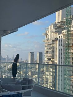 a woman standing on top of a balcony next to a tall building with lots of windows