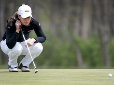 a woman kneeling down to put her golf ball on the green