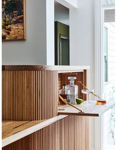 a wooden shelf with bottles and glasses on it in front of a painting hanging on the wall