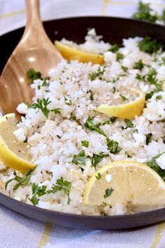 rice with lemons and parsley in a skillet on a table cloth next to a wooden spoon