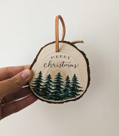 a hand holding a christmas ornament with pine trees on it and the words merry christmas