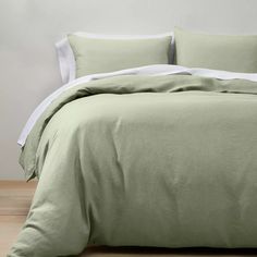 a bed with green linens and white sheets in a bedroom setting on a wooden floor