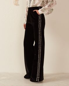 A person is dressed in black Charlie Rodeo Velvet Pant, showcasing a row of decorative buttons down the sides, paired with a floral long-sleeved top. They are standing indoors against a light-colored wall. Alix Of Bohemia, Velvet Pant, Velvet Pants, Leather Pieces, Studded Leather, Cotton Velvet, Slim Pants, Moda Operandi, Rodeo