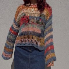 a woman standing in front of a white wall wearing a multicolored knit sweater