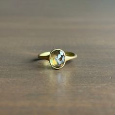 a yellow gold ring with an oval cut stone on it's side sitting on a wooden surface