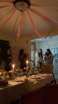 people standing around a dining room table with candles in the middle and decorations on the ceiling