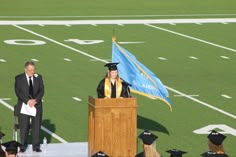 a woman standing at a podium in front of a flag on top of a football field