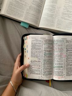 an open bible on top of a bed next to a person's hand holding it