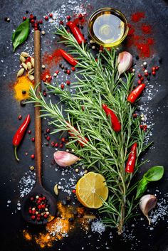 herbs and spices on a black background with pepper, lemon, rosemary, garlic, salt and pepper