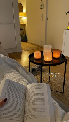 an open book sitting on top of a bed next to two lit candles and a coffee table