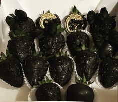 there are black strawberries in the box with gold decorations on them, and one is shaped like an elephant