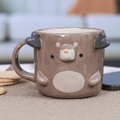 a coffee mug with a bear face on it next to crackers and a cell phone