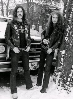 two men standing next to each other in front of a car on snow covered ground