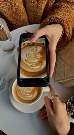 a woman is holding up her phone to take a photo of coffee art on the table