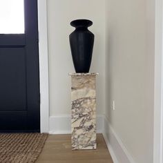 a black vase sitting on top of a marble block in the middle of a room