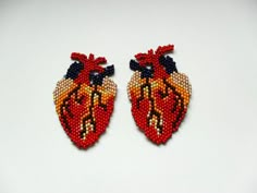 two beaded heart shaped brooches sitting on top of a white table next to each other