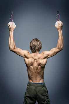 a man with no shirt holding two cell phones in his hands while standing against a gray background