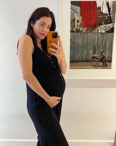 a pregnant woman taking a selfie with her cell phone in front of a painting