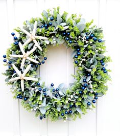 a wreath with starfishs and blue berries hanging on a white wooden door frame