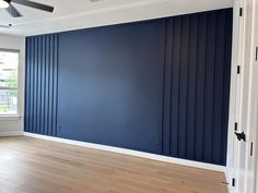 an empty room with blue walls and wood flooring in the foreground, there is a ceiling fan on the far wall