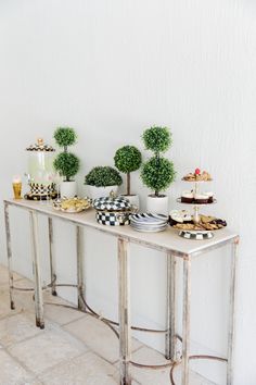 a table topped with plates and cakes covered in green topiary trees next to a white wall