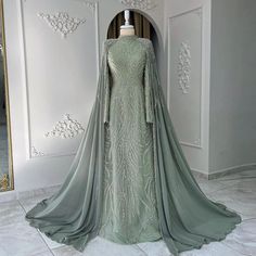 Experience the elegance and grace of our Dreamy Vow Luxury Evening Dress. With intricate beaded detailing, a stunning sage green color and a flowing cape, this dress is perfect for Muslim women seeking a luxurious and modest look. Complete with long sleeves, the perfect choice for any Arabic Dubai wedding or party. Elegant Green Gown With Cape Sleeves, Evening Dress With Cape, Custom Flower Girl Dress, Yellow Evening Dresses, Dubai Women, Silver Evening Dress, Muslimah Wedding Dress, Purple Evening Dress, Muslim Evening Dresses