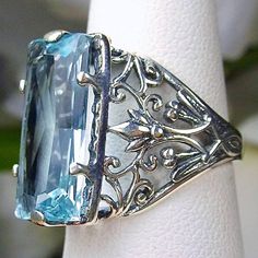 Sky Blue Aquamarine Ring Baguette Design#32 Introducing the Baguette D32, a stunning piece of wearable art that pays homage to the opulent Victorian era. Crafted with meticulous attention to detail, this exquisite filigree Antique reproduction in sterling silver is sure to captivate anyone with a love for vintage-inspired jewelry. At its center, lies a flawless 7ct sky blue gemstone, radiating a dazzling hue that catches the light with every movement. The baguette rectangle-cut gemstone measures Blue Evening Rings, Leaf Filigree, Blue Aquamarine Ring, Ring Baguette, Baguette Ring, Filigree Jewelry, Vintage Inspired Jewelry, Victorian Design, Aquamarine Ring