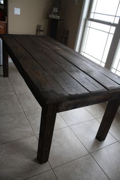 a wooden table sitting on top of a white tile floor next to a large window