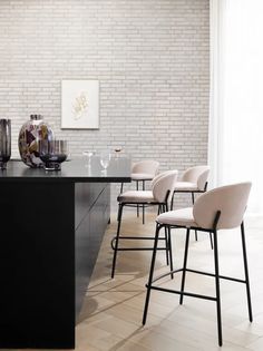 a modern kitchen with white brick walls and black countertops, chairs are lined up in front of the island