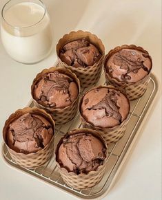 six chocolate muffins sitting on a cooling rack next to a glass of milk