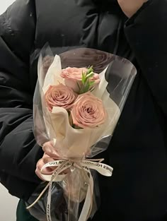 a person holding a bouquet of roses in their hands and wearing a black jacket with a white ribbon