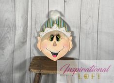 a wooden stool with a paper doll on it's head sitting next to a wood wall