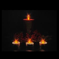 three lit candles sitting on top of a table next to some grapes and berries in the dark