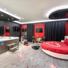 a bedroom decorated in red and black with a heart shaped bed, tv, desks, chairs, and other accessories