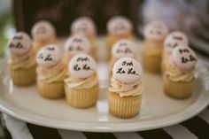 small cupcakes with white frosting and black writing on them sitting on a plate