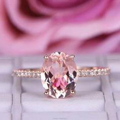 a pink diamond ring sitting on top of a white surface with flowers in the background