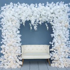 a couch sitting under a white flower covered arch in front of a blue wall with flowers on it