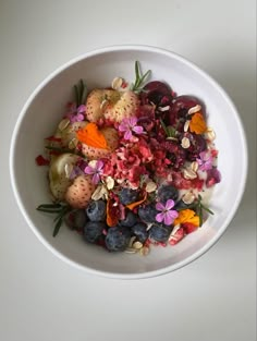 a white bowl filled with fruit and veggies on top of a white table