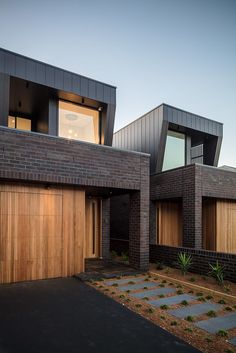 two garages with wooden doors and brick walls in front of a house at dusk