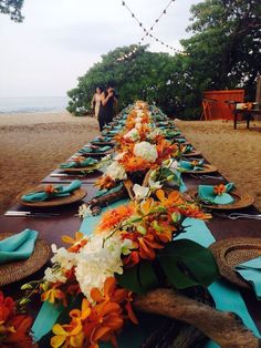 a long table is set up on the beach for an outdoor dinner party with orange and white flowers