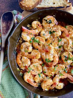 a skillet filled with shrimp and bread on top of a table next to utensils