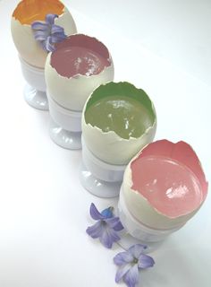 three small containers filled with different colored creams on top of a white table next to purple flowers