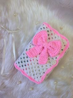 a pink and white crocheted case with a bow on it's side