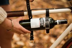 a person is holding a wine bottle in their hand while standing next to a bike