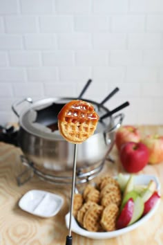 a waffle on a stick next to some apples and other foods in front of a pot